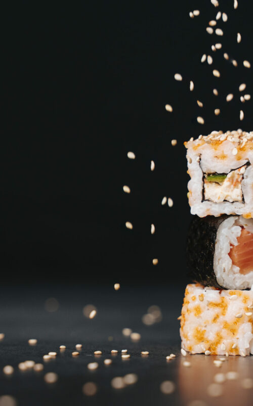 Japanese sushi rolled and placed one on top of the other while rice is spilled. Dark background. Front view. Copy Space.