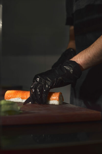 Sushi Chef Slices fresh Salmon on the sushi bar, Chef cutting salmon fillet at professional kitchen, sushi with salmon and avocado. Sushi menu. Japanese food.